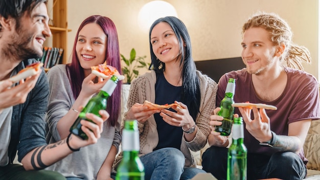 Foto jóvenes divirtiéndose bebiendo cerveza con pizza y rugiendo en la casa