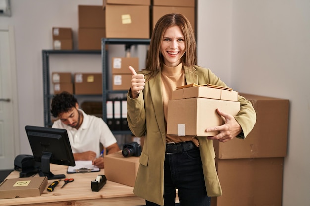 Jóvenes dos personas que trabajan en el comercio electrónico de pequeñas empresas sonriendo felices y con el pulgar positivo haciendo un excelente y signo de aprobación