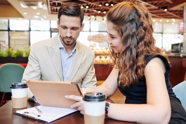 Jóvenes emprendedores con tablet PC discutiendo nuevas ideas para el desarrollo de proyectos en una reunión en el café