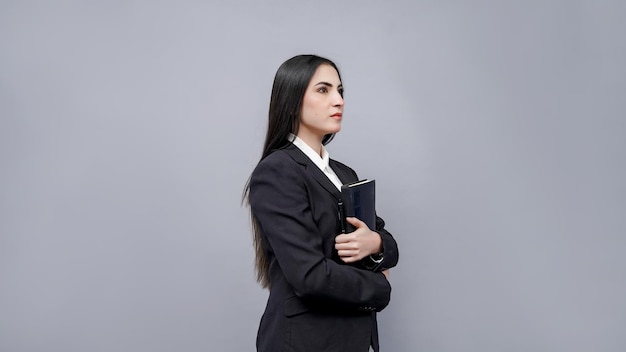 Jóvenes empresarias sosteniendo libro mirando a la derecha vistiendo abrigo negro modelo paquistaní indio