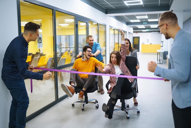 Jóvenes empresarios alegres corriendo en sillas de oficina y riendo Actividad divertida