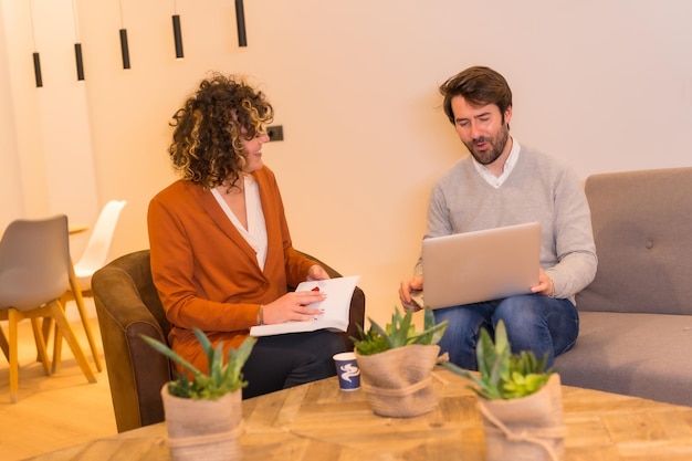 Jóvenes empresarios caucásicos en una reunión de negocios en sofás con una computadora y un cuaderno