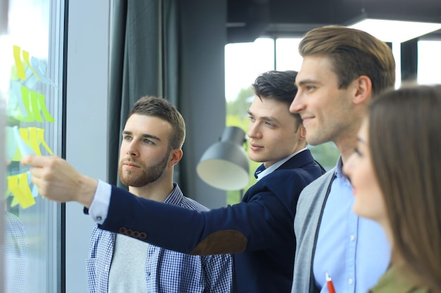 Jóvenes empresarios creativos de inicio en reunión en la oficina moderna haciendo planes y proyectos con pegatinas de poste en vidrio