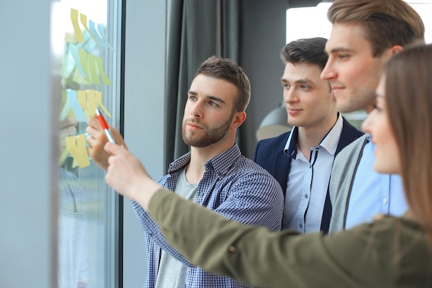 Jóvenes empresarios creativos de inicio en reunión en la oficina moderna haciendo planes y proyectos con pegatinas de poste en vidrio