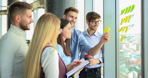 Jóvenes empresarios creativos que se inician en la reunión en la oficina moderna haciendo proyectos de planes con pegatinas de poste en vidrio