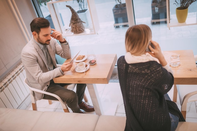 Jóvenes empresarios en un descanso en un café. Hombre pensativo trabajando en tableta y bebiendo café. Mujer con teléfono inteligente. Enfoque selectivo. Centrarse en el hombre de negocios.