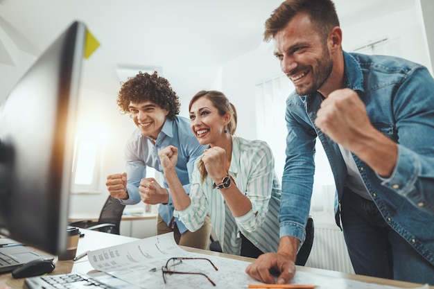 Jóvenes empresarios exitosos celebrando el éxito mientras trabajan en un nuevo proyecto en la oficina informal.