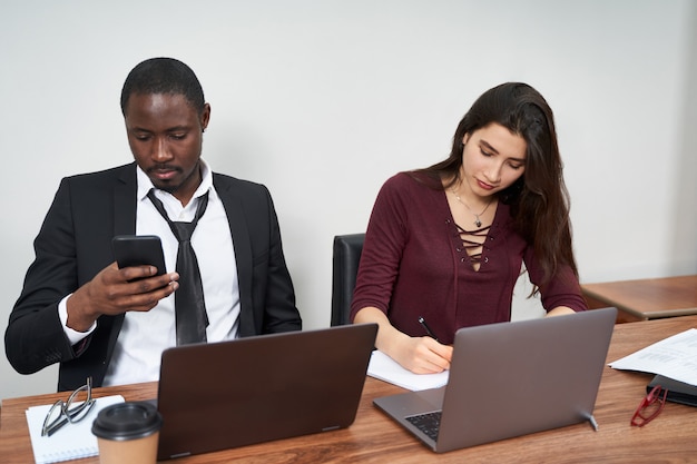 Jóvenes empresarios felices trabajando juntos en la oficina moderna, trabajo en equipo multiétnico. Hombre llamando con teléfono inteligente