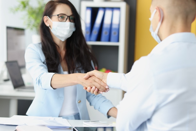 Jóvenes empresarios en máscaras médicas se dan la mano en la mesa de trabajo