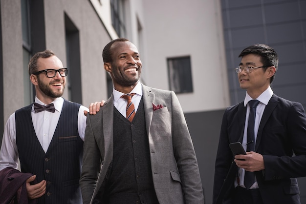 Jóvenes empresarios multiétnicos con estilo en ropa formal caminando al aire libre, reunión de equipo de negocios