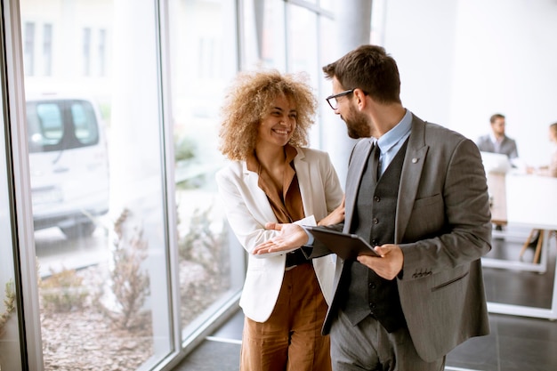 Jóvenes empresarios multiétnicos de pie juntos y hablando en la oficina moderna