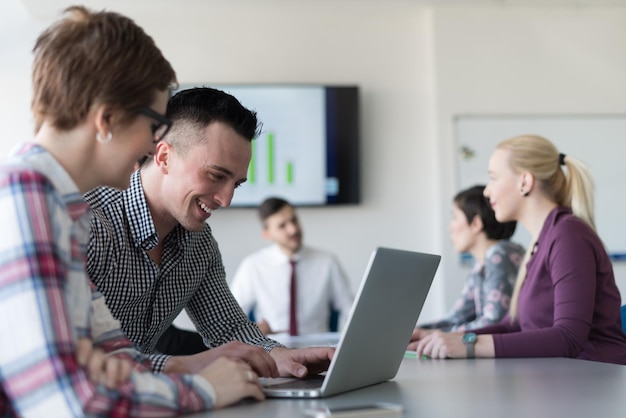 jóvenes empresarios de nueva creación, pareja que trabaja en una computadora portátil, grupo de empresarios reunidos en segundo plano en el interior de la oficina