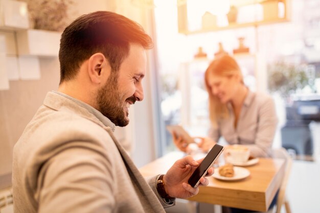 Jóvenes empresarios sonrientes en un descanso en un café. Hombre que usa un teléfono inteligente y lee un mensaje de Internet. Mujer trabajando en tableta. Enfoque selectivo. Centrarse en primer plano, en el hombre de negocios.