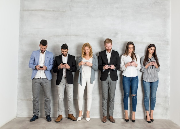 Jóvenes empresarios con teléfono móvil de pie junto a la pared