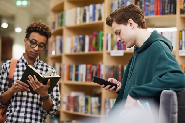 Jóvenes estudiantes muchachos que eligen literatura en la biblioteca