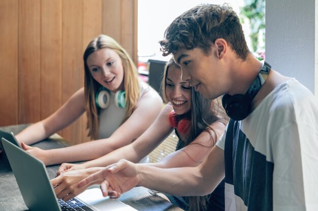 Los jóvenes estudiantes trabajan juntos usando una computadora portátil y amigos sentados usando una computadora y una tableta digital