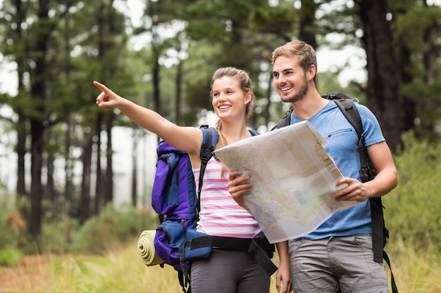 Jóvenes excursionistas felices apuntando en la distancia con un mapa