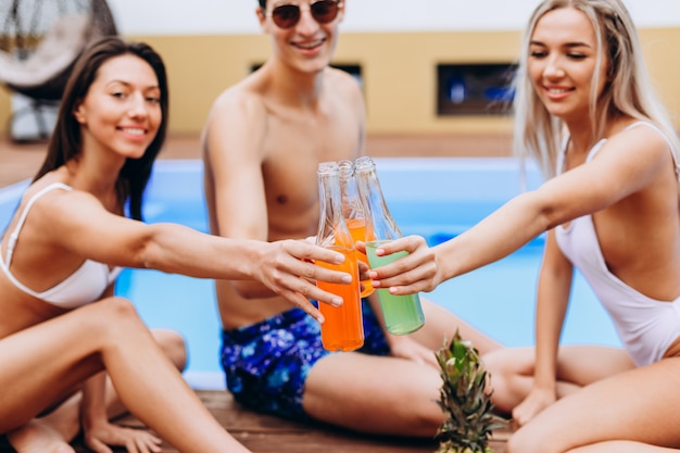 Jóvenes felices con bebidas en la fiesta de verano cerca de la piscina
