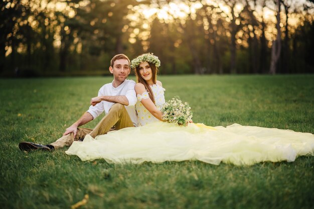 Jóvenes felices recién casados sentados en la hierba en el parque al atardecer