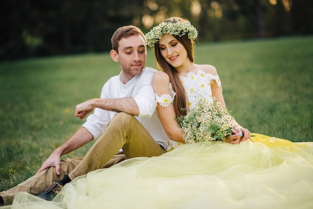 Jóvenes felices recién casados sentados en la hierba en el parque al atardecer