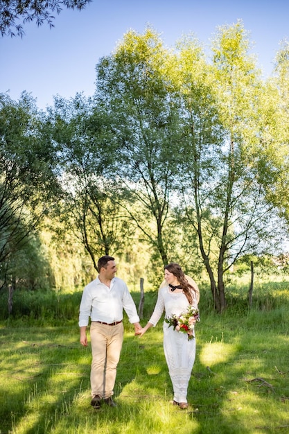 Jóvenes felices vestidos de novia caminan por el prado y se miran unos a otros