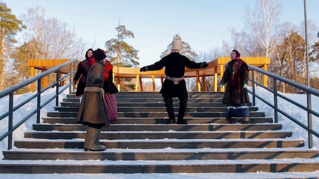 Jóvenes folclóricos rusos con botas de fieltro bailan en las escaleras en el parque de invierno