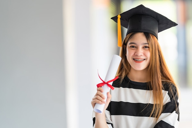 Jóvenes graduados universitarios asiáticos en toga de graduación y birrete tienen un certificado de grado