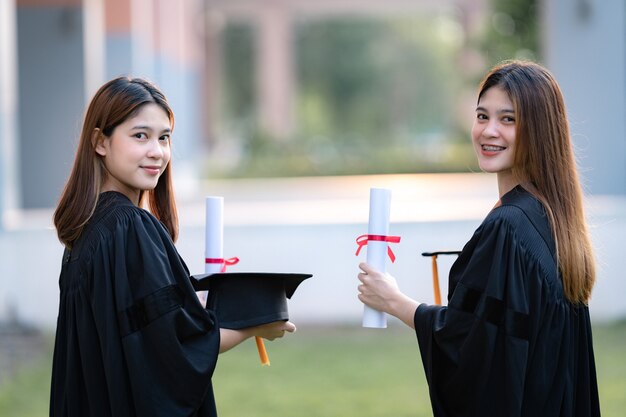 Jóvenes graduados universitarios de mujeres asiáticas felices en toga de graduación y birrete tienen un certificado de grado celebran el logro educativo en el campus universitario. Educación foto de stock