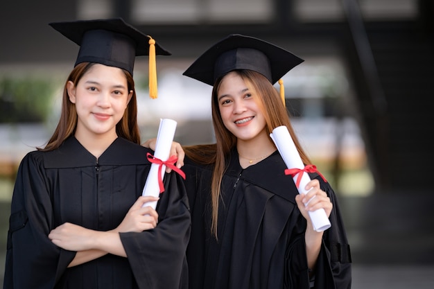 Jóvenes graduados universitarios de mujeres asiáticas felices en toga de graduación y birrete tienen un certificado de grado celebran el logro educativo en el campus universitario. Educación foto de stock