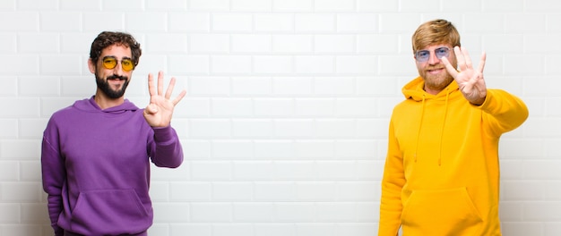 Jóvenes guapos, sonrientes y de aspecto amistoso, que muestran el número cuatro o cuarto con la mano hacia adelante, contando contra la pared de azulejos blancos