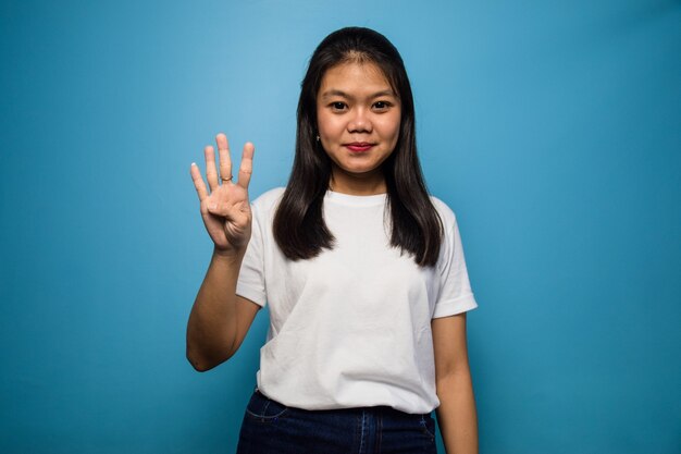 Jóvenes hermosas mujeres asiáticas con camiseta blanca con fondo azul aislado cuatro signo 4