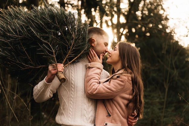Jóvenes hermosos amantes felices hombre y mujer historia de amor en invierno con un árbol de Navidad vivo en un bosque de pinos al sol