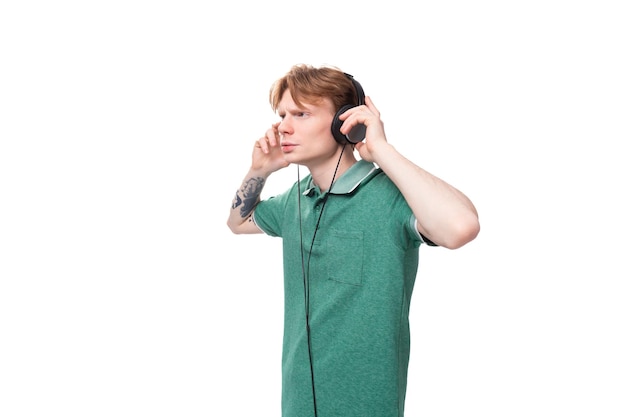 Jóvenes hombres pelirrojos especialistas en una camiseta verde escucha música en auriculares con cable durante un