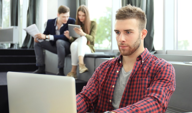 Los jóvenes inteligentes utilizan dispositivos mientras trabajan duro en la oficina moderna. Hombre joven que trabaja en su computadora portátil.
