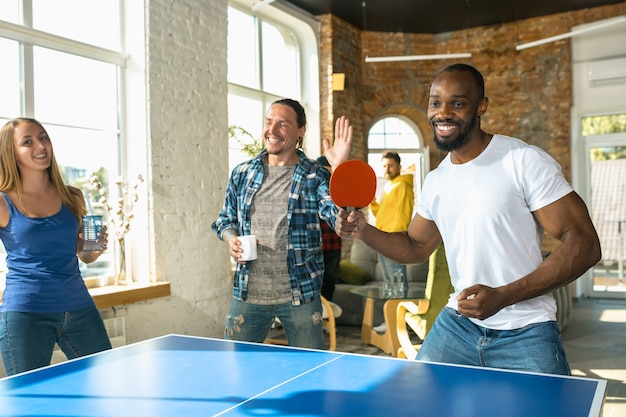 Jóvenes jugando al tenis de mesa en el lugar de trabajo, divirtiéndose