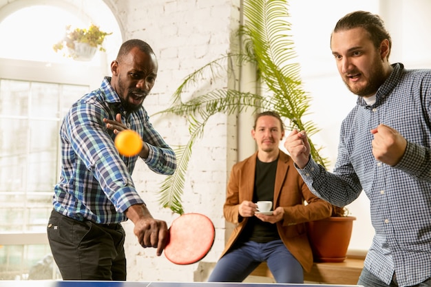 Jóvenes jugando al tenis de mesa en el lugar de trabajo, divirtiéndose