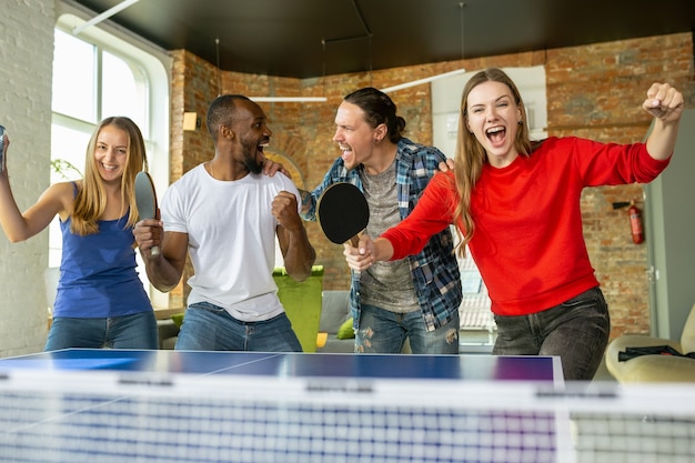 Jóvenes jugando al tenis de mesa en el lugar de trabajo, divirtiéndose