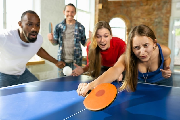 Jóvenes jugando al tenis de mesa en el lugar de trabajo, divirtiéndose