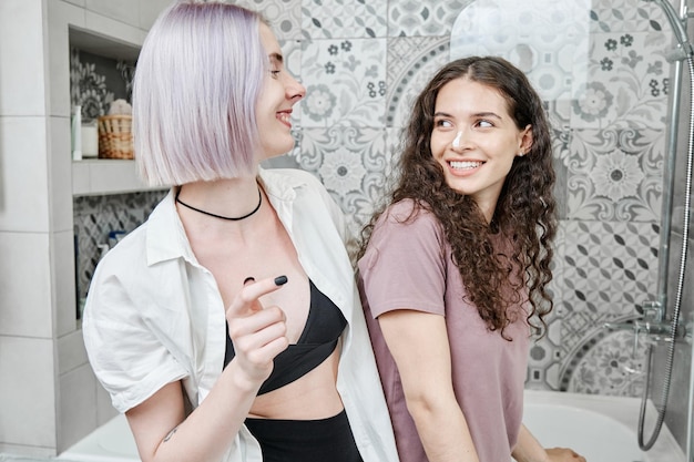 Jóvenes lesbianas caucásicas felices en ropa de casa riéndose mientras disfrutan juntas de la rutina matutina