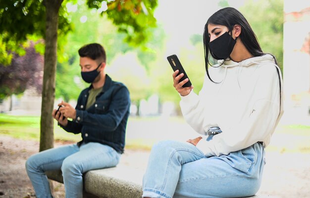 Los jóvenes mantienen el distanciamiento social debido al coronavirus mientras usan su teléfono al aire libre en un parque