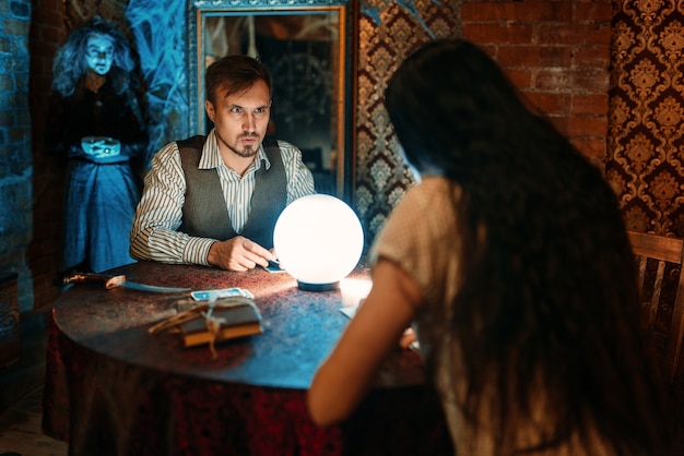 Jóvenes en la mesa con bola de cristal en sesión espiritual, bruja aterradora. Hembra pronosticadora llama a los espíritus