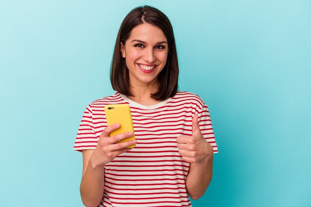 Jóvenes mujeres caucásicas sosteniendo teléfono móvil aislado sonriendo y levantando el pulgar hacia arriba