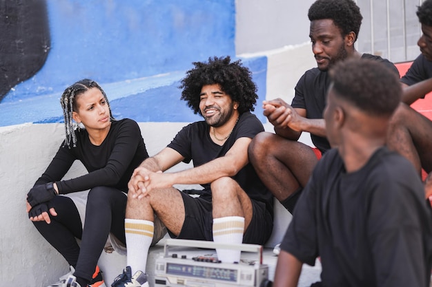 Jóvenes multirraciales divirtiéndose escuchando música de un boombox vintage después de un partido de baloncesto