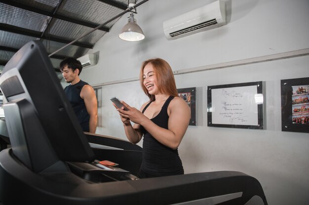 Jóvenes musculosas asiáticas corren en cinta rodante con smartphone