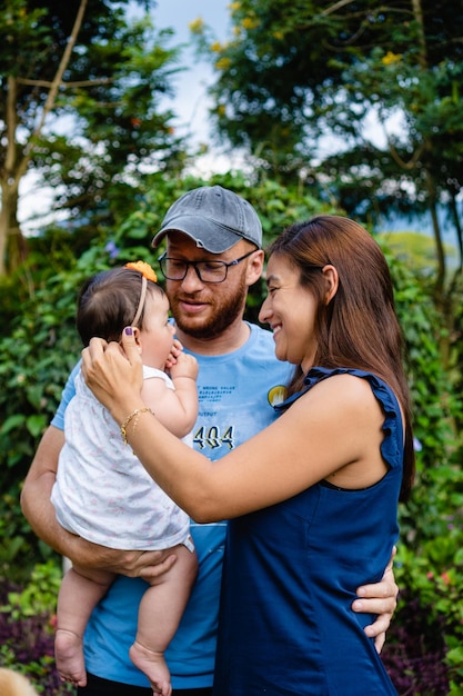 Jóvenes padres latinos sonriendo sosteniendo a su bebé recién nacido en una foto vertical del parque