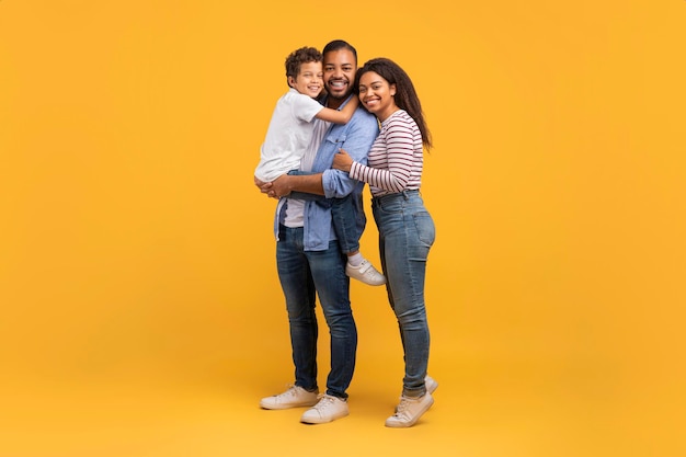 Jóvenes padres negros felices con su hijo pequeño posando sobre un fondo amarillo