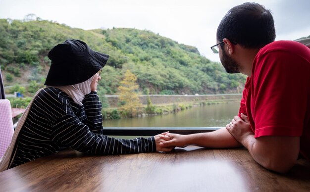 Foto jóvenes parejas musulmanas se enamoran mientras miran el lago natural desde la mesa del restaurante durante las vacaciones sosteniendo la otra mano