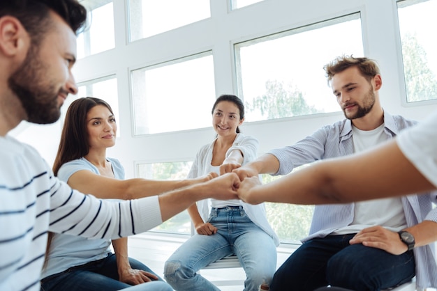 Jóvenes positivos felices sentados en círculo y haciendo una actividad de trabajo en equipo mientras aprenden a trabajar juntos