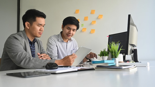 Jóvenes programadores que trabajan en computadoras y tabletas en el lugar de trabajo de la oficina moderna.