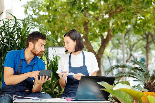 Jóvenes propietarios de pequeñas empresas discutiendo los gastos y ganancias del mes pasado cuando se sientan a la mesa en la cafetería al aire libre